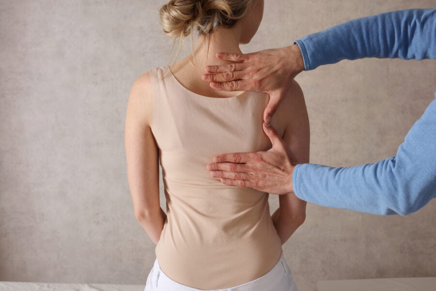 A practitioner evaluating a woman’s spinal alignment and posture by hand as part of a personalized corrective exercise program - Corrective Exercise Programs